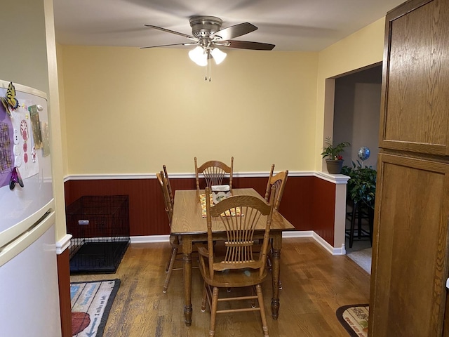dining room with a wainscoted wall, a ceiling fan, and wood finished floors