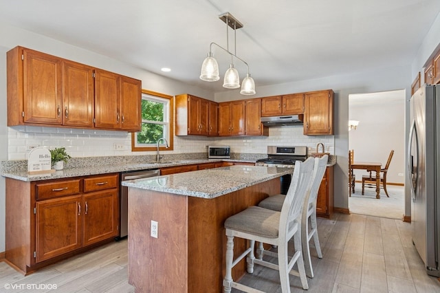 2020 Saint Andrews Dr, Plainfield, IL 60586 - kitchen with under cabinet range hood, appliances with stainless steel finishes, brown cabinets, backsplash, and light wood-type flooring