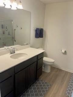 bathroom featuring toilet, wood finished floors, vanity, a stall shower, and a chandelier