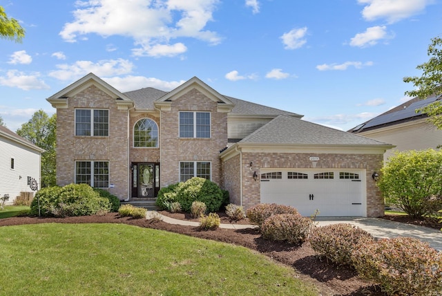 traditional home featuring an attached garage, brick siding, a front yard, concrete driveway, and a shingled roof
