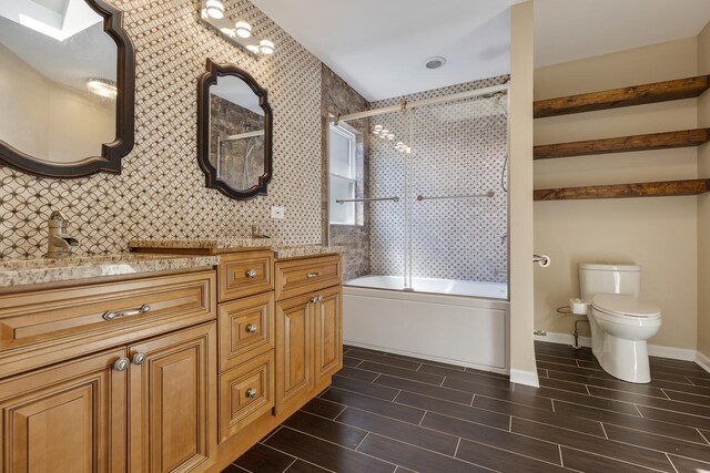 bathroom featuring toilet, wood finish floors, vanity, combined bath / shower with glass door, and baseboards