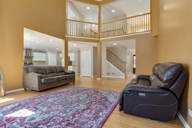 living area featuring light wood-style floors, stairs, a high ceiling, baseboards, and recessed lighting