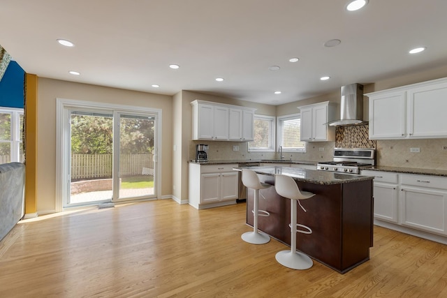 kitchen featuring wall chimney range hood, stove, a sink, light wood-style flooring, and recessed lighting