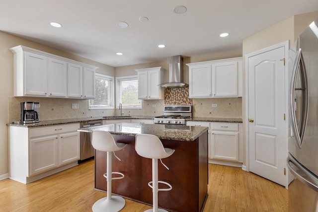 kitchen with wall chimney range hood, appliances with stainless steel finishes, a sink, white cabinets, and recessed lighting