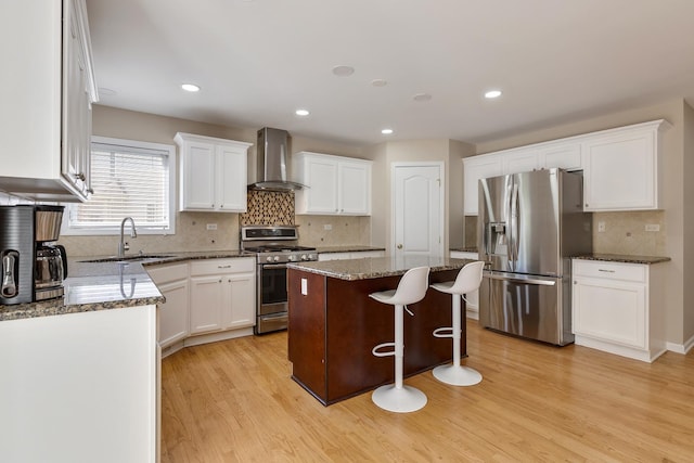 kitchen with stainless steel appliances, wall chimney exhaust hood, a sink, backsplash, and light wood finished floors