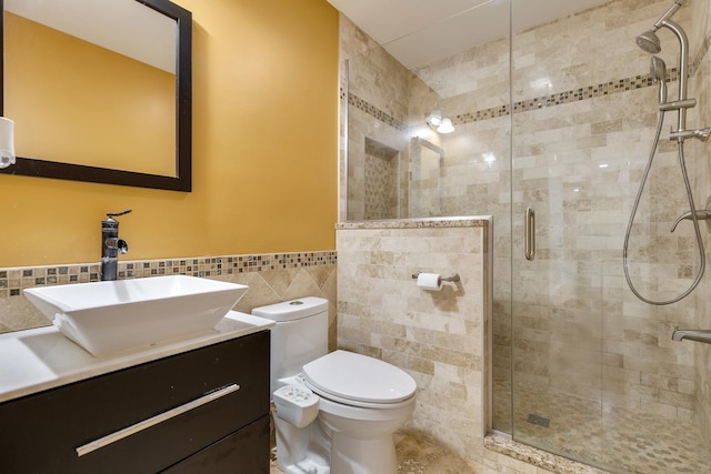 full bath featuring tile walls, a stall shower, toilet, vanity, and wainscoting