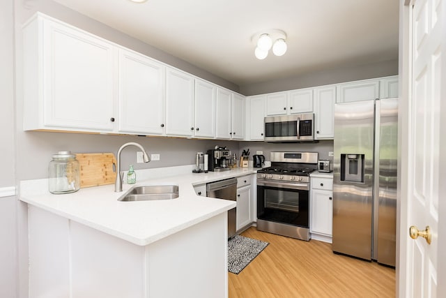 kitchen with appliances with stainless steel finishes, a sink, light countertops, light wood finished floors, and white cabinetry