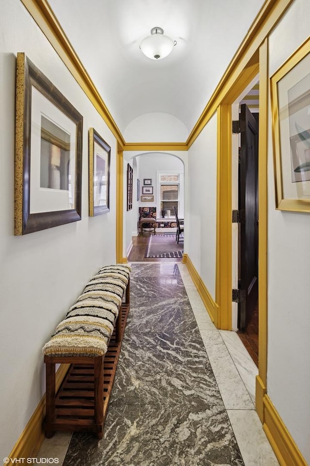 hallway featuring baseboards, marble finish floor, lofted ceiling, and arched walkways