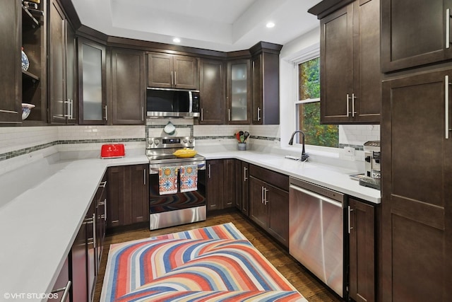 kitchen featuring recessed lighting, dark brown cabinets, a sink, backsplash, and appliances with stainless steel finishes