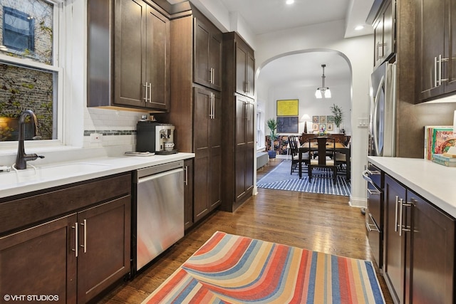 kitchen featuring a sink, tasteful backsplash, dishwasher, arched walkways, and light countertops