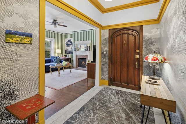 foyer with a ceiling fan, crown molding, a lit fireplace, and wood finished floors