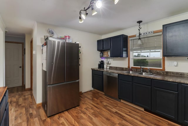 kitchen featuring appliances with stainless steel finishes, a sink, ornamental molding, dark countertops, and dark wood-style flooring