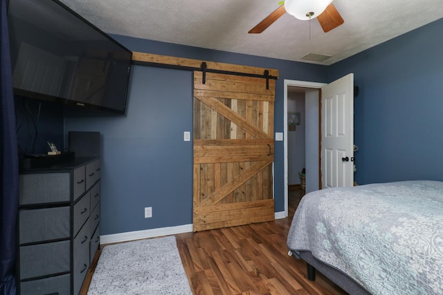bedroom featuring a barn door, baseboards, dark wood-style flooring, and ceiling fan