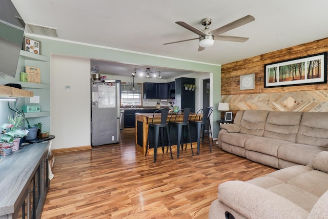 living room featuring wood walls, a ceiling fan, light wood finished floors, and baseboards