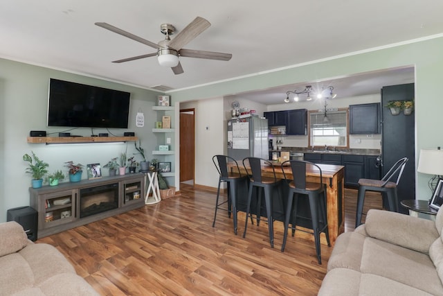 living area with a ceiling fan, light wood-type flooring, and ornamental molding