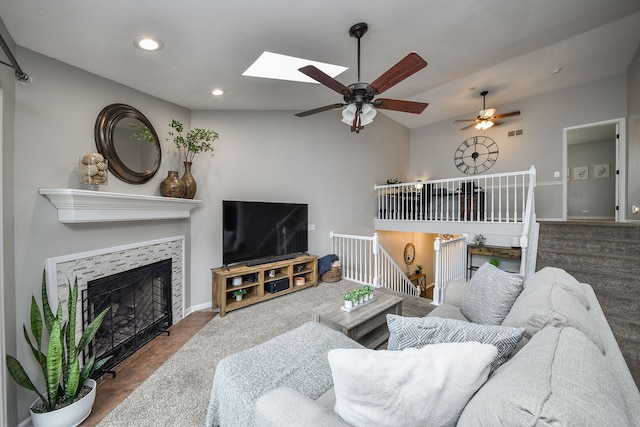 living area featuring a ceiling fan, a skylight, recessed lighting, a fireplace, and vaulted ceiling