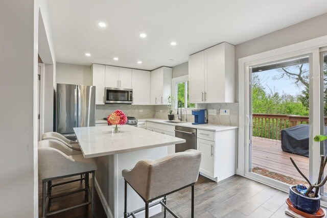kitchen with appliances with stainless steel finishes, a breakfast bar, a kitchen island, light countertops, and wood finished floors