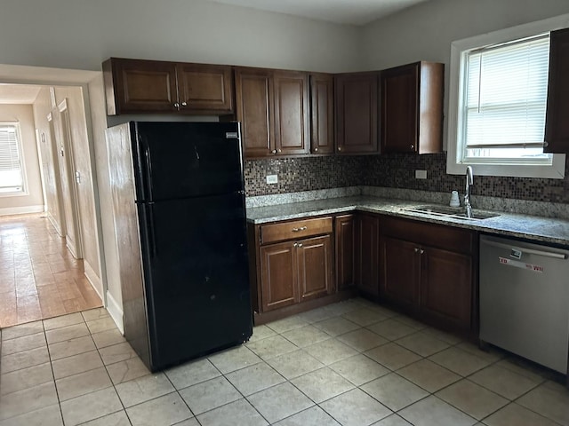 kitchen with light tile patterned floors, a sink, freestanding refrigerator, stainless steel dishwasher, and decorative backsplash