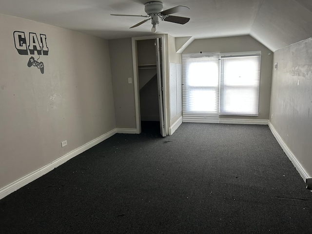 unfurnished bedroom featuring lofted ceiling, dark carpet, baseboards, and a ceiling fan
