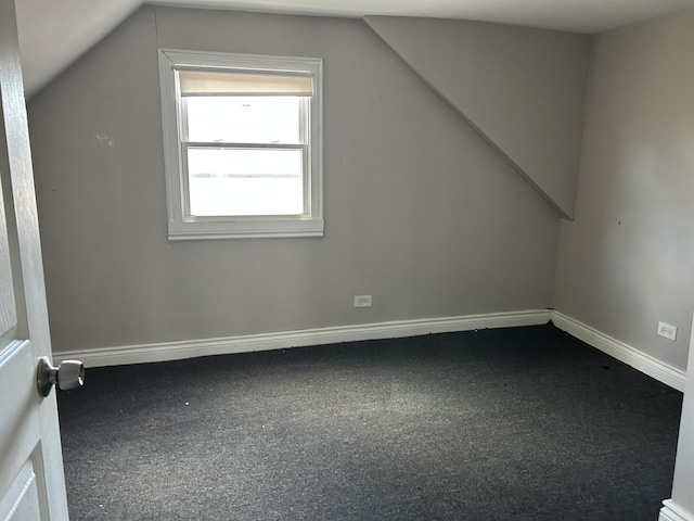 bonus room featuring lofted ceiling, dark colored carpet, and baseboards