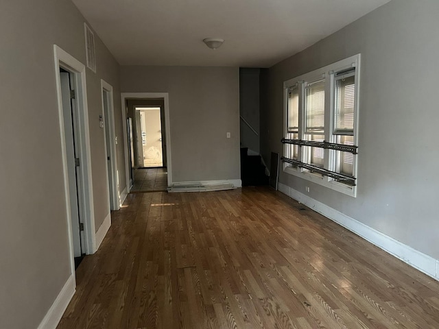 unfurnished room with visible vents, wood finished floors, baseboards, and stairs