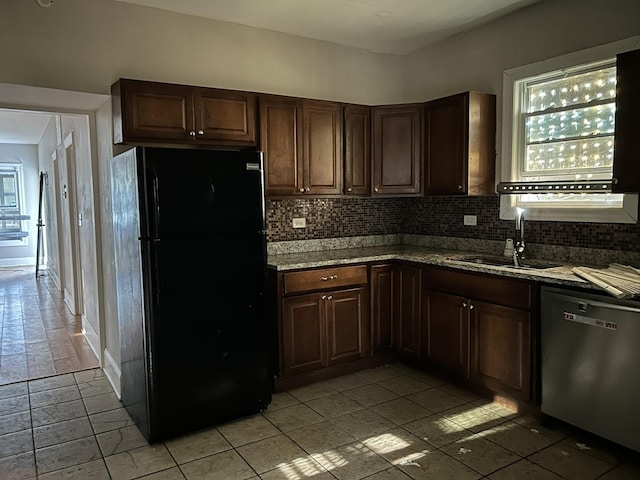 kitchen with freestanding refrigerator, dishwasher, light tile patterned floors, a sink, and decorative backsplash