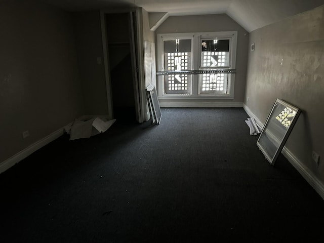 empty room featuring vaulted ceiling, dark colored carpet, and baseboards