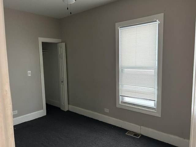 empty room featuring baseboards, a ceiling fan, visible vents, and dark carpet