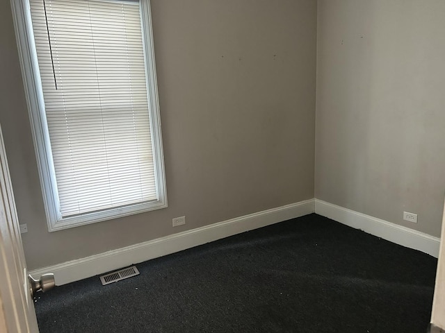 spare room with baseboards, dark colored carpet, and visible vents