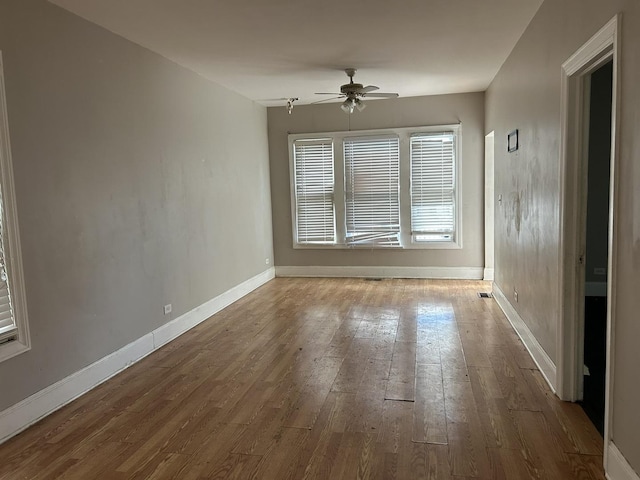 empty room featuring wood-type flooring, baseboards, a ceiling fan, and visible vents