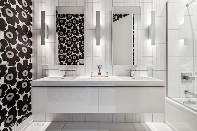 bathroom with double vanity, tile walls, enclosed tub / shower combo, and a sink