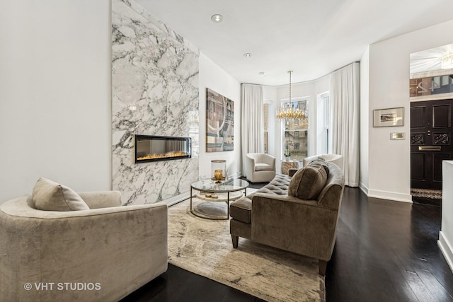 living room with a premium fireplace, an inviting chandelier, baseboards, and wood finished floors