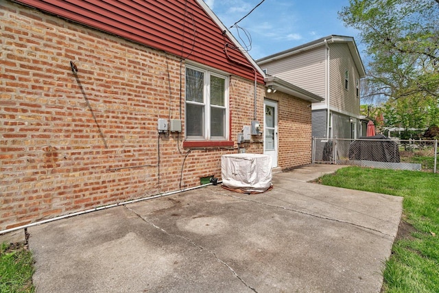 view of property exterior featuring brick siding, a patio area, and fence