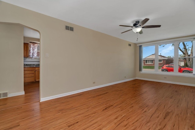 unfurnished room with light wood finished floors, a ceiling fan, baseboards, and arched walkways