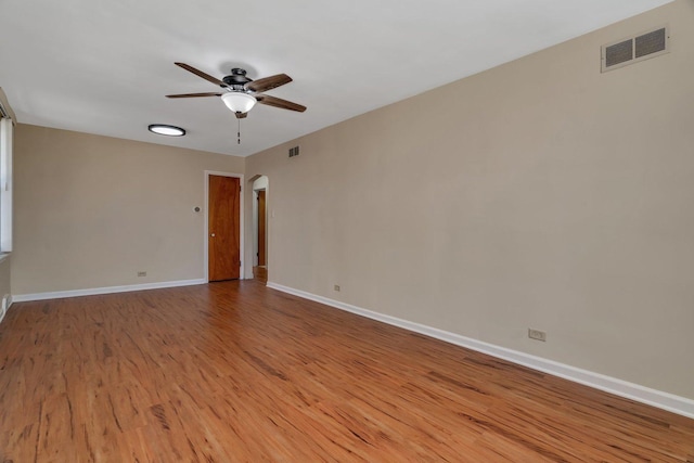 unfurnished room featuring ceiling fan, wood finished floors, baseboards, and arched walkways
