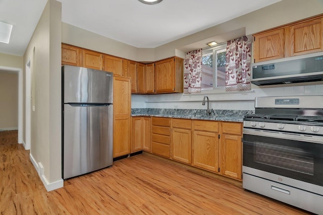 kitchen featuring appliances with stainless steel finishes, light wood-style flooring, a sink, brown cabinets, and baseboards