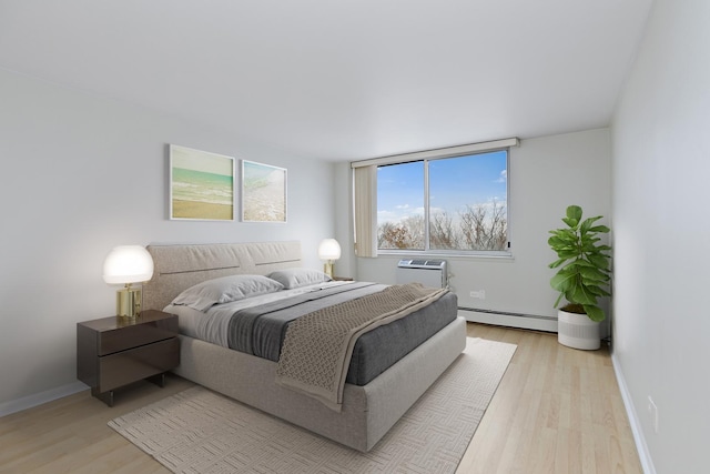 bedroom featuring a baseboard heating unit, light wood-style floors, an AC wall unit, and baseboards