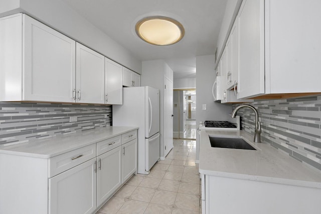 kitchen featuring white appliances, light tile patterned floors, white cabinetry, decorative backsplash, and a sink