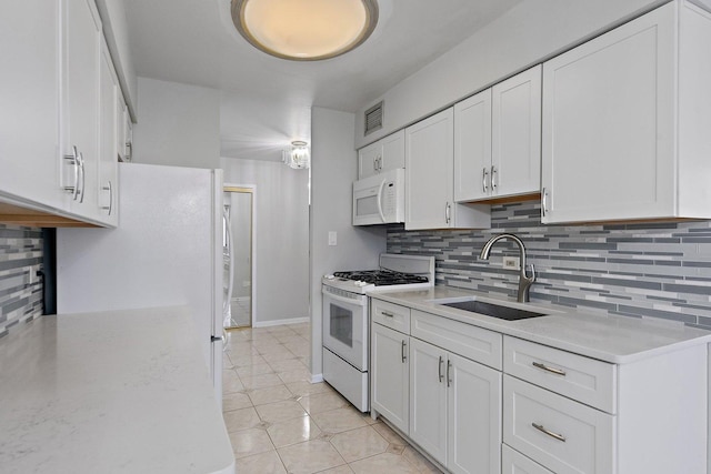 kitchen featuring white appliances, a sink, white cabinets, decorative backsplash, and light tile patterned floors