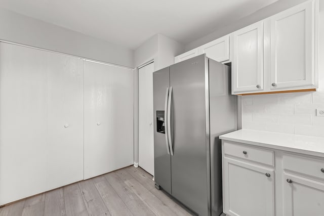 kitchen featuring stainless steel fridge with ice dispenser, light wood-style flooring, light countertops, white cabinets, and decorative backsplash