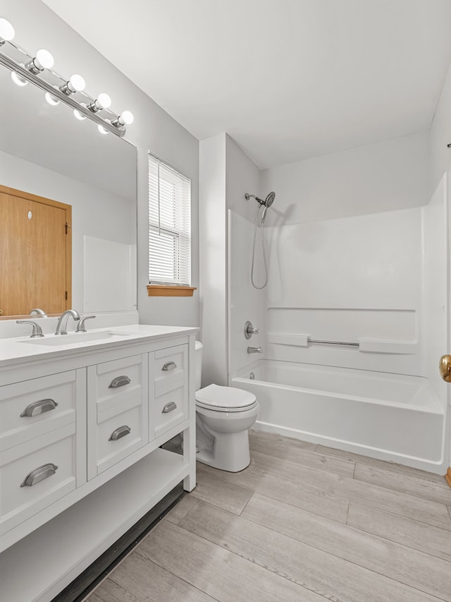 full bath with washtub / shower combination, toilet, wood finished floors, and vanity
