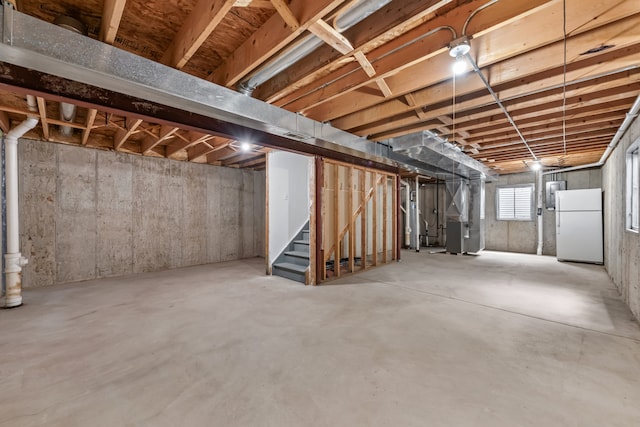 basement featuring freestanding refrigerator, heating unit, and stairway