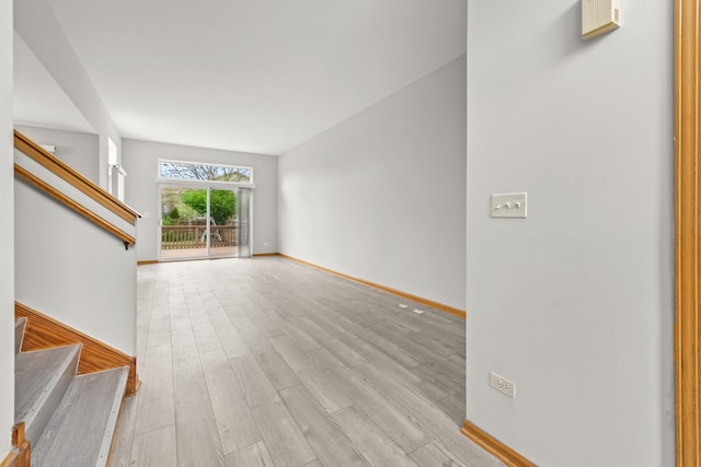 unfurnished living room with stairway, light wood-style floors, and baseboards
