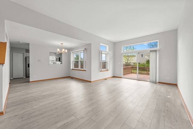 unfurnished living room featuring a chandelier, baseboards, and light wood-style floors
