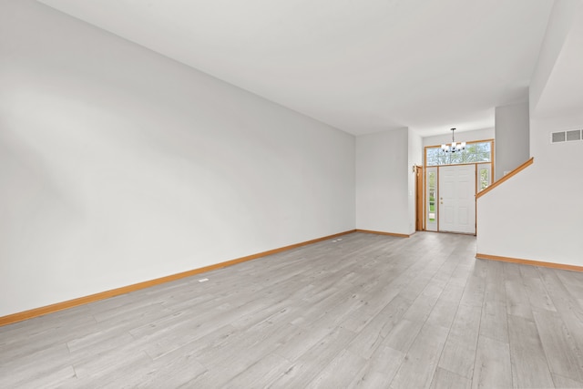 unfurnished living room with a chandelier, light wood-style floors, and baseboards