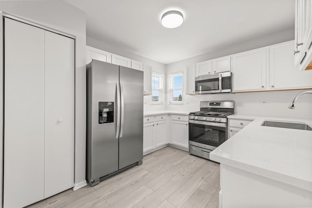 kitchen with stainless steel appliances, a sink, white cabinetry, and light wood finished floors
