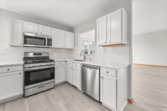 kitchen featuring appliances with stainless steel finishes, a sink, light wood finished floors, and white cabinetry