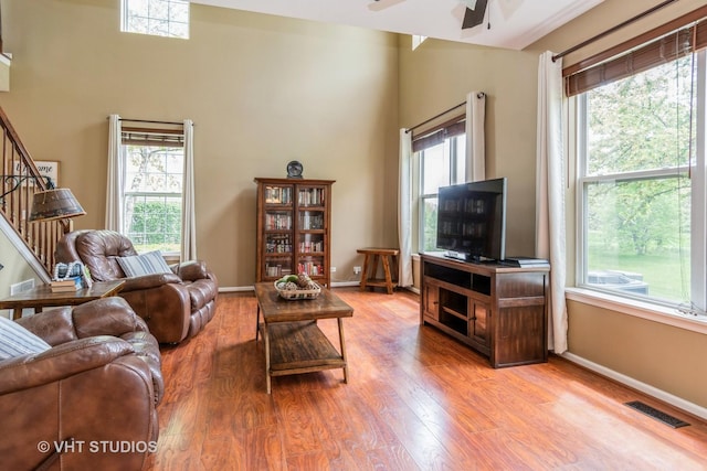 living room featuring a ceiling fan, wood finished floors, stairway, baseboards, and a high ceiling