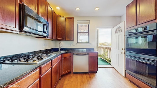 kitchen with black appliances, a sink, light wood finished floors, recessed lighting, and dark stone counters
