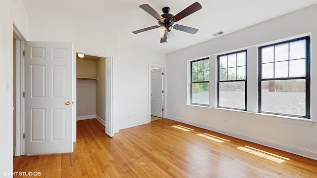 unfurnished bedroom with baseboards, light wood-style flooring, a walk in closet, a closet, and a ceiling fan